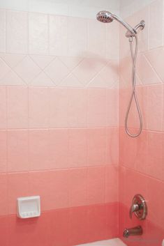 a bathroom with pink and white tiles on the walls, shower head and hand held soap dispenser