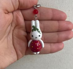 a hand holding a keychain with a small white rabbit wearing a red dress