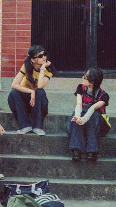 three people sitting on steps with luggage and backpacks in front of them, one woman is talking to the other