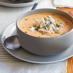 there is a bowl of soup on the table with silver spoons and napkins