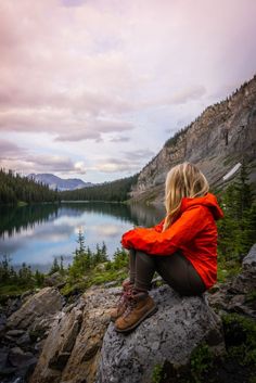 a woman sitting on top of a rock next to a lake