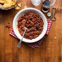 a bowl of chili and chips on a wooden table