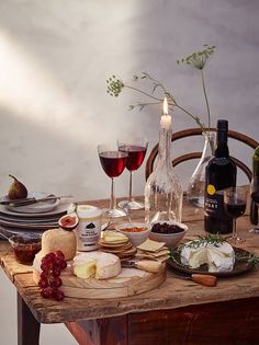 a wooden table topped with wine glasses and cheeses next to bottles of red wine