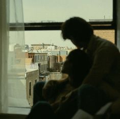 two people sitting in front of a window looking out at the city below and buildings behind them