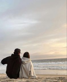 two people sitting on the beach looking out at the ocean