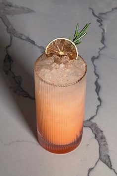 a drink with an orange garnish on the rim sits on a marble surface