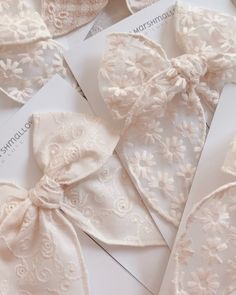 some white cards with bows on them and laces around the edges are laying on top of each other