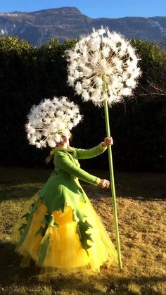 a woman in a green dress holding a large dandelion with white flowers on it