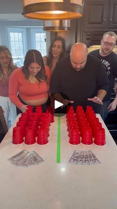 a group of people standing around a table with red cups on it and one person pointing at the cup