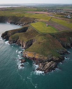 an aerial view of the ocean and coastline near some cliffs with grass growing on them