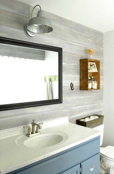 a white toilet sitting under a bathroom mirror next to a blue vanity and wooden wall