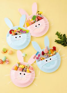 three paper plates with bunny ears and candy in them on a yellow surface next to green plants