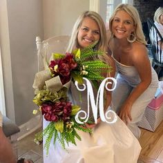 two beautiful women standing next to each other in front of a chair holding bouquets