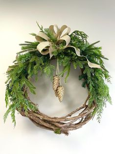 a wreath with pine cones and greenery hanging on the wall next to a white wall