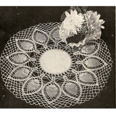 a white doily with flowers on it and a vase in the middle, sitting on a black surface