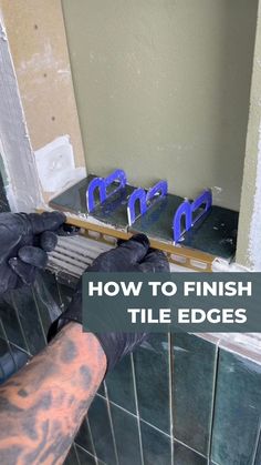 a man in black gloves is fixing the tile on a bathroom wall with blue scissors