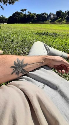 a person laying in the grass with a tattoo on their arm and palm tree behind them