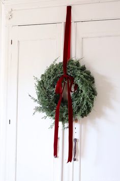 a wreath hanging on the front door with a red ribbon around it and a pair of scissors next to it