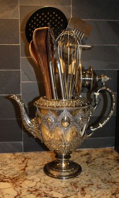 a silver teapot with utensils in it on top of a countertop