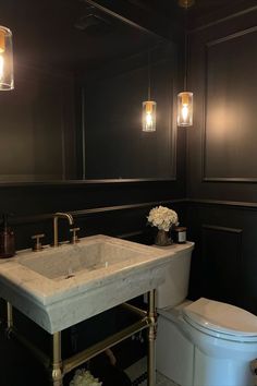 a white toilet sitting next to a sink in a bathroom under two hanging light bulbs