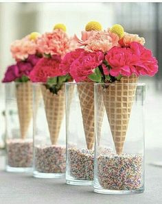 three ice cream cones filled with sprinkles and flowers in vases on a table