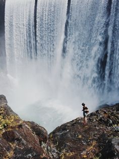 a person standing at the edge of a waterfall looking down on water falling from it