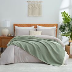 a bed with a green blanket on top of it next to a potted plant