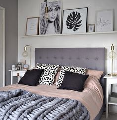 a bed with pillows and blankets on it in a bedroom next to two framed pictures