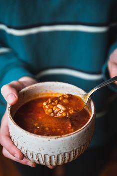 a person holding a bowl of soup with a spoon in it