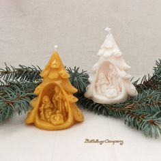 two small candles sitting next to each other on top of a pine tree covered in snow