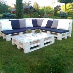 a couch made out of wooden pallets in the grass with pillows on top of it