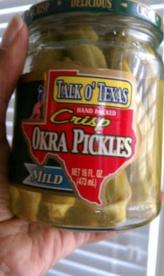 a hand holding a jar of pickles in front of a window with the words talk o'texas on it