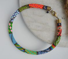 a bracelet made with multicolored beads on a marble slab next to a plant