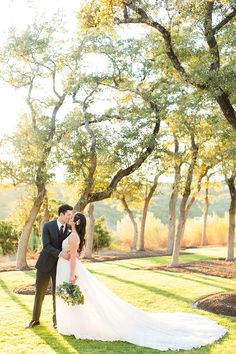 a bride and groom kissing in front of trees at their outdoor wedding venue on a sunny day