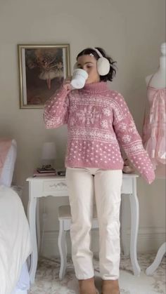 a woman drinking from a cup while standing in front of a white table with headphones on