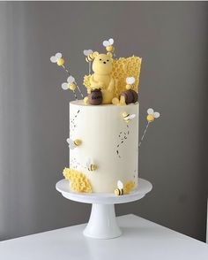 a white cake with yellow decorations and bees on the top is sitting on a pedestal