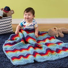 a baby is sitting on the floor with a crocheted blanket and teddy bear