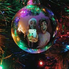 an ornament hanging from a christmas tree with two people holding a cell phone