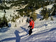 a man riding skis down the side of a snow covered slope with trees in the background