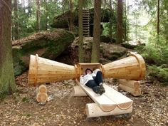 a woman laying on top of a wooden bench next to a giant telescope in the woods