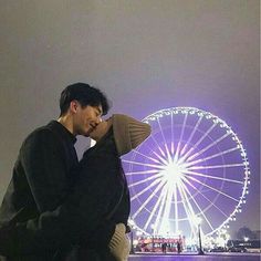 a man and woman kissing in front of a ferris wheel