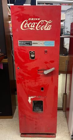 an old coca - cola machine sitting on the floor