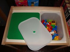 a plastic container filled with legos on top of a wooden table next to a cutting board