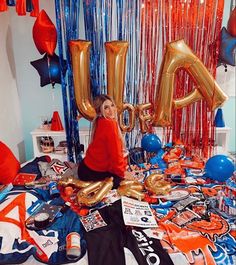 a woman sitting on top of a bed surrounded by balloons and streamers in the shape of letters