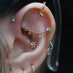 a woman wearing ear piercings with green and white stones