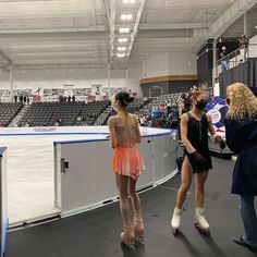 two women in short dresses are standing near an ice rink and talking to each other