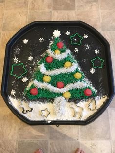 someone standing next to a decorated christmas tree on a black tray with white icing