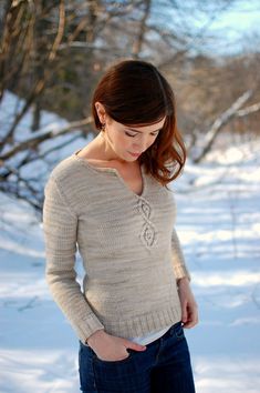 a woman standing in the snow with her hands on her hips, wearing a sweater and jeans