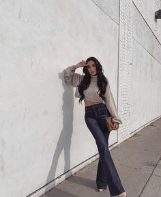 a woman leaning against a white wall with her hand on her hip and looking at the camera