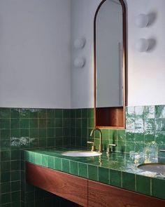 a green tiled bathroom with two sinks and a mirror